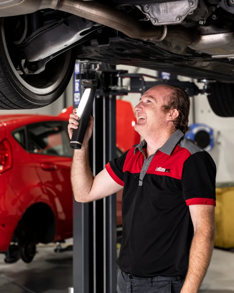 Mechanic inspecting European car's suspension system using diagnostic light at Brisbane workshop